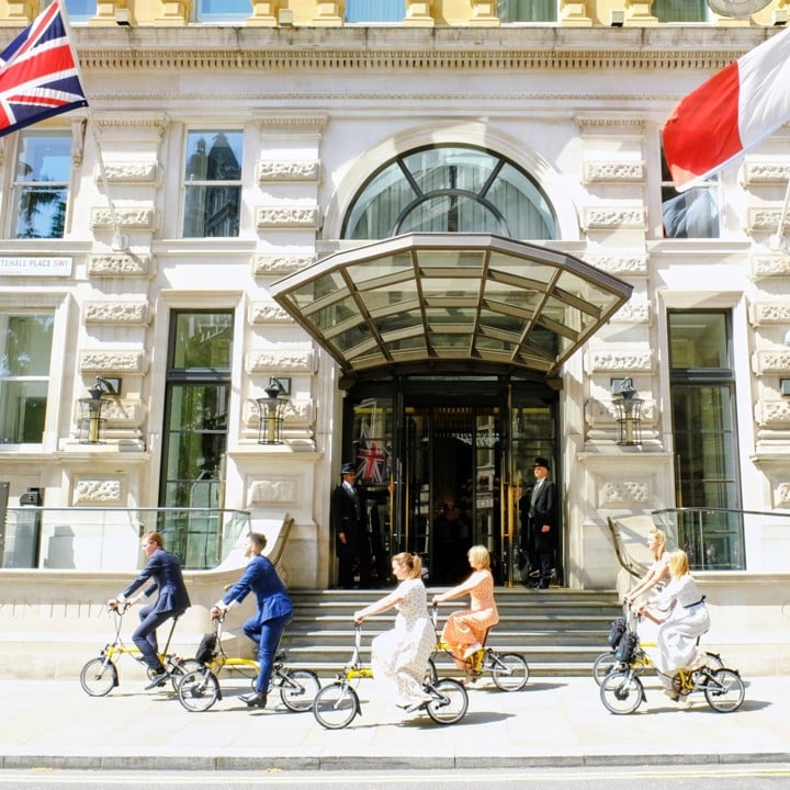 Five people riding Brompton bikes outside hotel entrance