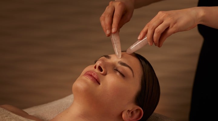 Spa therapist holding rose quartz crystals on woman's forehead lying down